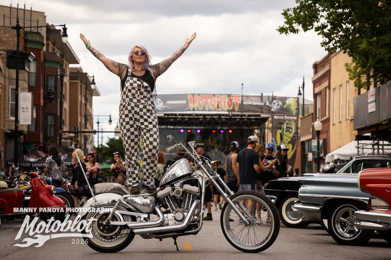 MOTOBLOT Valhalla 2026 winner Morgan Michelle stands triumphantly on The Glitterus, her 2001 Harley-Davidson Sportster, during the festival.